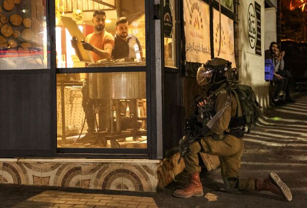 Trabalhadores de padaria observam agente das forças de segurança israelenses, em meio ao conflito israelo-palestino na cidade de Hebron, em Israel, em 5 de novembro de 2021. - Sputnik Brasil