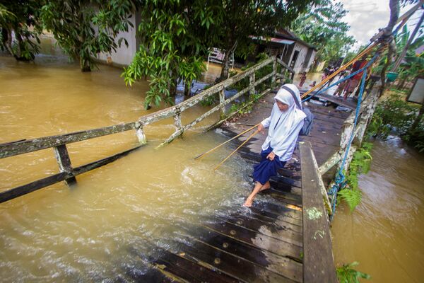 Estudante caminha por uma ponte atingida pelo transbordamento de um rio após enchentes, Indonésia, 17 de novembro de 2021. - Sputnik Brasil