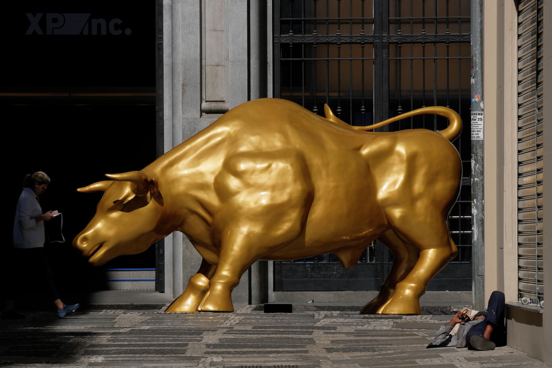 Homem sem-teto dorme perto do Touro de Ouro, réplica do Touro de Wall Street, símbolo do mercado financeiro, fora da B3, São Paulo, 17 de novembro de 2021 - Sputnik Brasil, 1920, 27.12.2021