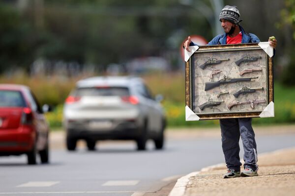 Antonio, imigrante colombiano, segura moldura com réplicas de armas antigas na tentativa de as vender em uma rua em Brasília. - Sputnik Brasil