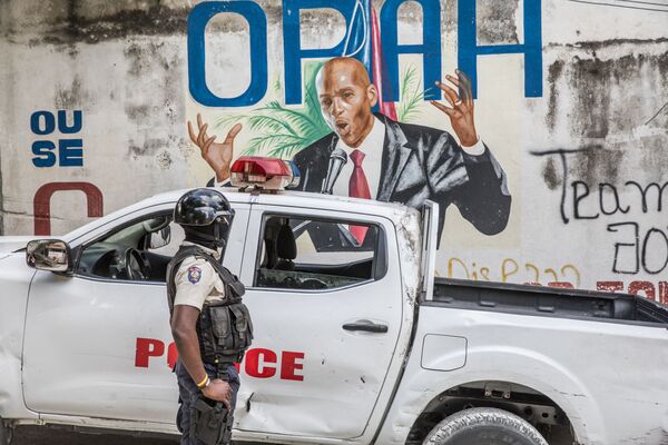Policial em frente a um muro pintado com o retrato do ex-presidente haitiano, Jovenel Moise, após agentes do FBI e equipes de criminalística realizarem buscas em sua residência, em Porto Príncipe, 15 de julho de 2021. - Sputnik Brasil