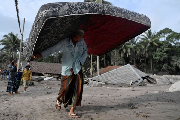 Morador carrega cama durante evacuação do assentamento de Sumber Wuluj, do distrito de Lumajang, Indonésia, 5 de dezembro de 2021, após erupção do vulcão - Sputnik Brasil