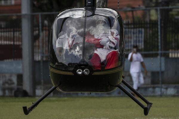 Um homem vestido de Papai Noel chega de helicóptero para uma celebração de Natal na Vila Olímpica na favela Vila Kennedy, no Rio de Janeiro. - Sputnik Brasil