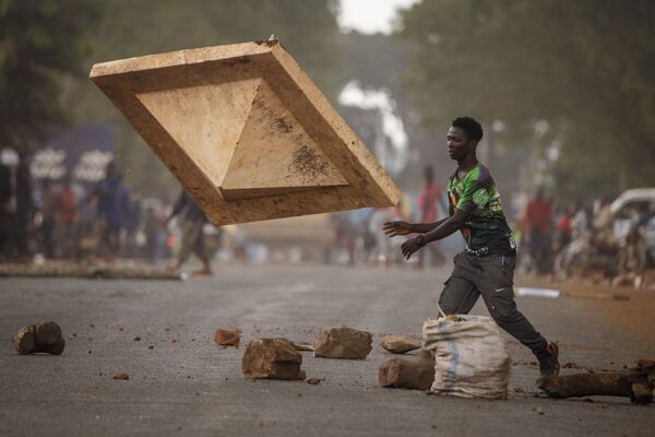 Um apoiante do partido da oposição Plataforma de Unidade Nacional  bloqueia uma estrada enquanto policiais dispersam manifestantes em Uganda. - Sputnik Brasil