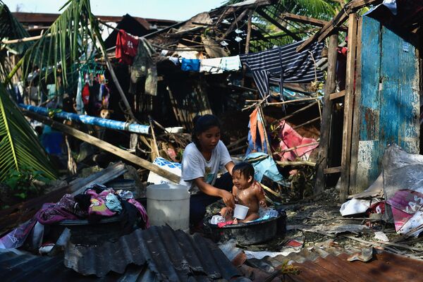 Mulher cuida de seu bebê ao lado de sua casa destruída em resultado do furacão nas Filipinas, 18 de dezembro de 2021. - Sputnik Brasil