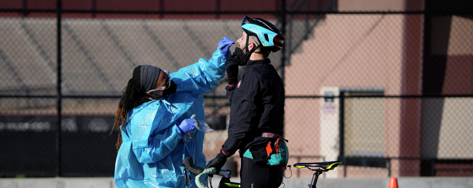 Um técnico médico realiza um teste de esfregaço nasal em um ciclista na fila de uma fila com motoristas em um local de testes COVID-19 perto do All City Stadium, 30 de dezembro de 2021 - Sputnik Brasil, 1920, 02.01.2022