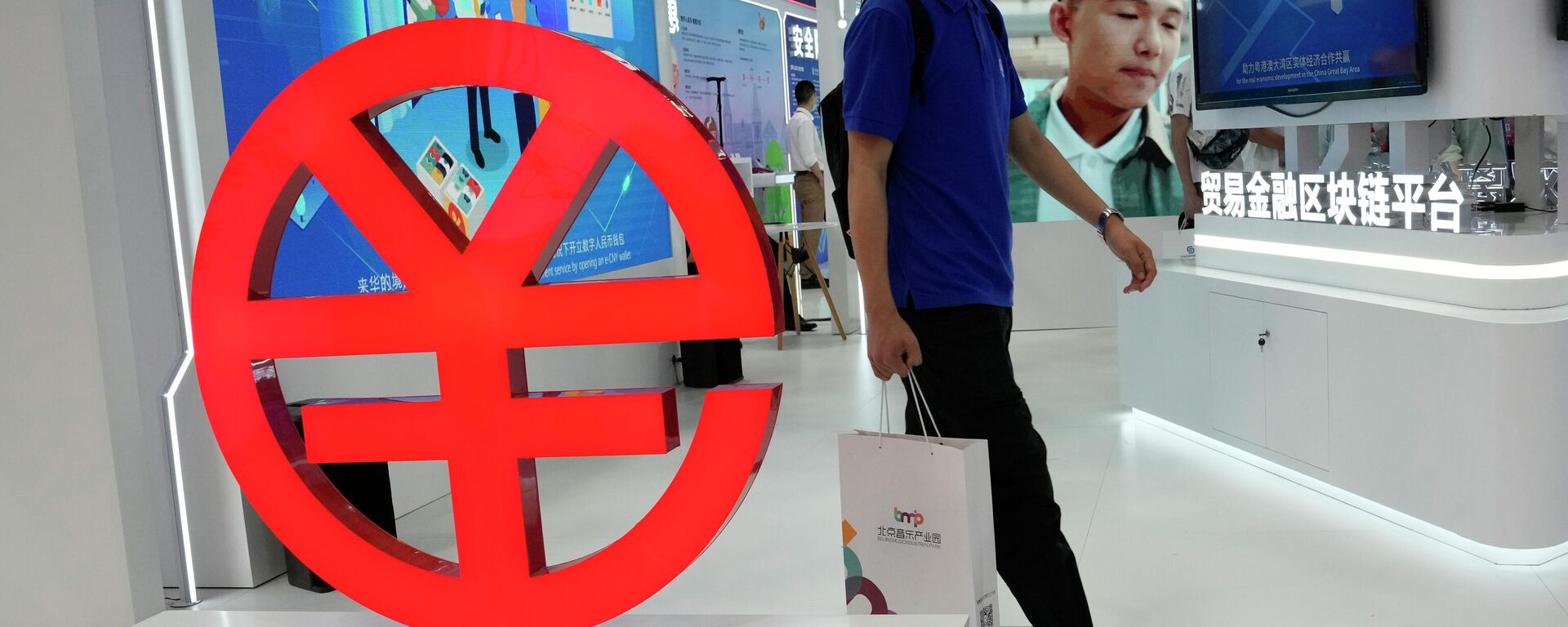Um visitante passa por um logotipo do e-CNY, uma versão digital do Yuan chinês, exibido durante uma feira comercial em Pequim, China, 5 de setembro de 2021 - Sputnik Brasil, 1920, 04.01.2022