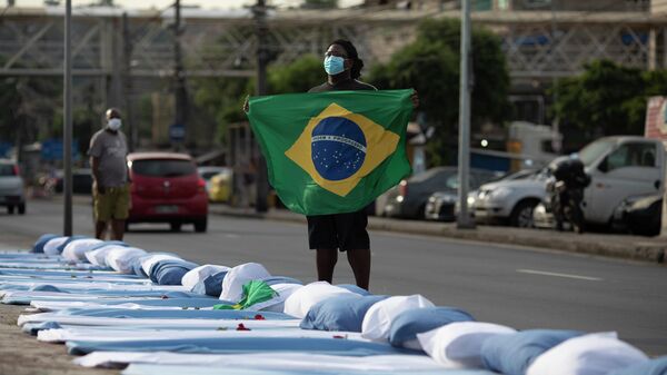 Manifestante segura bandeira nacional do Brasil ao lado de colchões com rosas simbolizando as vítimas da COVID-19, durante protesto em frente ao hospital Ronaldo Gazolla, no Rio de Janeiro, no Brasil, em 24 de março de 2021 - Sputnik Brasil