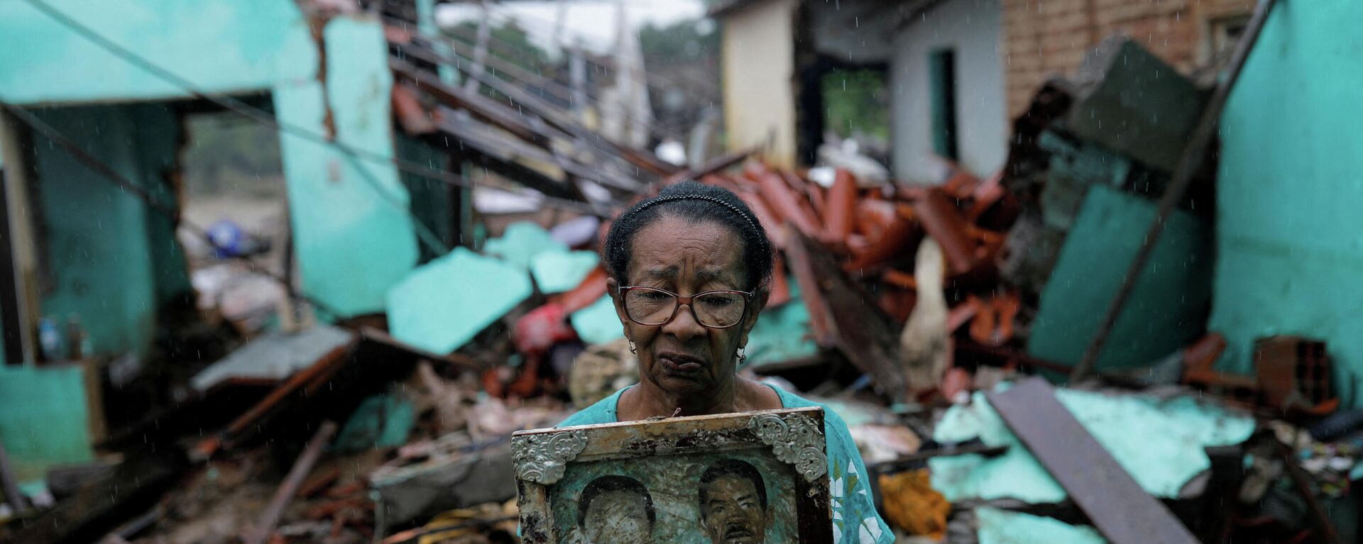 Em Itambé, no estado brasileiro da Bahia, Vitória Rocha, de 81 anos, segura uma foto de seus pais em frente aos escombros de sua casa destruída por enchentes, em 28 de dezembro de 2021 - Sputnik Brasil, 1920, 12.01.2022