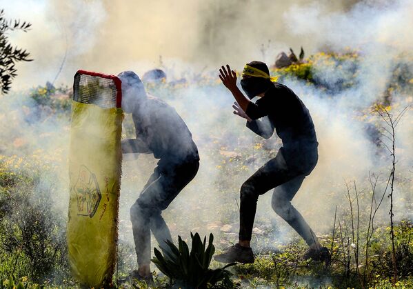 Jovens palestinos se escondem durante confrontos com forças de segurança de Israel após manifestação contra a expropriação de terras por Tel Aviv na Cisjordânia ocupada, 21 de janeiro de 2022 - Sputnik Brasil