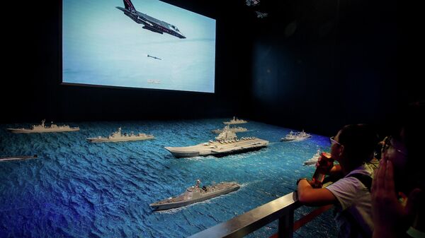 Visitantes assistem a uma tela de TV mostrando um avião F-35 da Força Aérea dos EUA disparando um míssil perto dos modelos do porta-aviões Liaoning com fragatas e submarinos da Marinha em exibição no museu militar em Pequim (foto de arquivo) - Sputnik Brasil