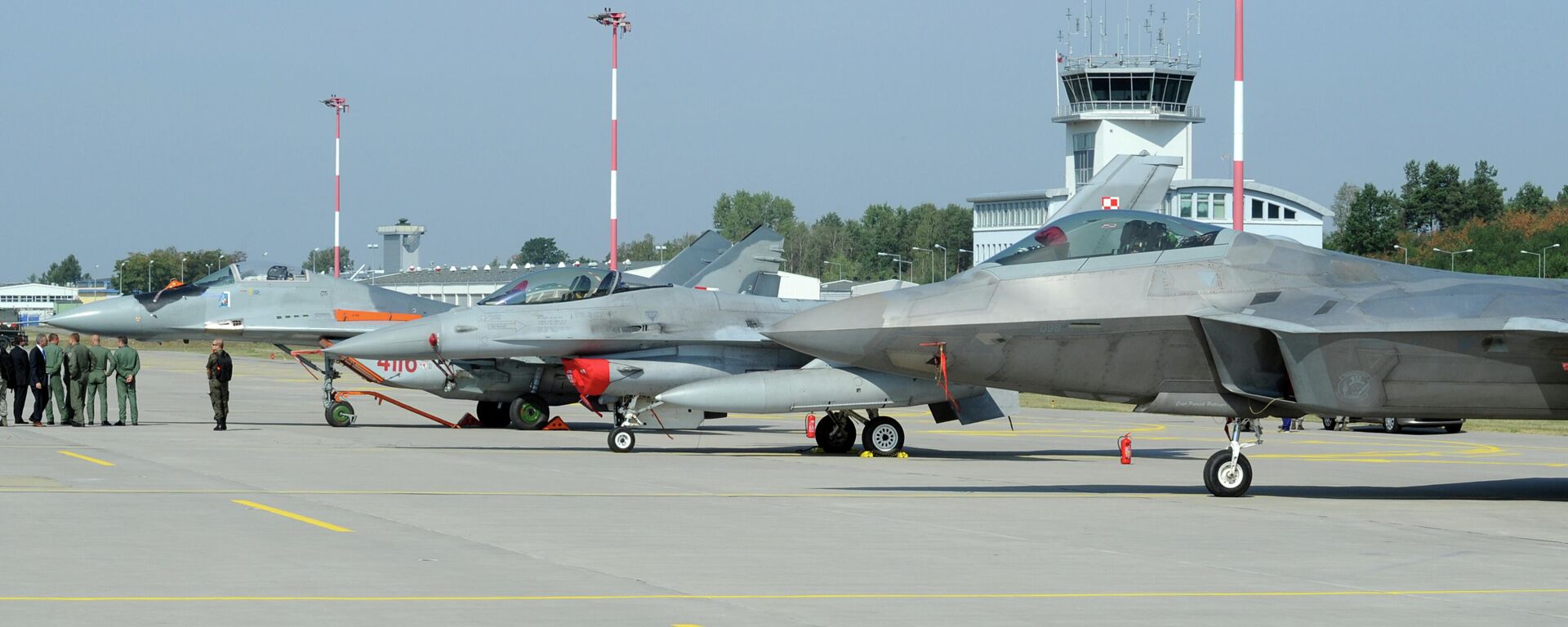 Autoridades passam por caças estacionados no pátio, um Mig-29 da Força Aérea Polonesa, à esquerda, um F-16 da Força Aérea Polonesa, ao centro e um F-22 Raptor dos EUA em uma base militar em Lask, Polônia, segunda-feira, 31 de agosto de 2015 - Sputnik Brasil, 1920, 09.03.2022