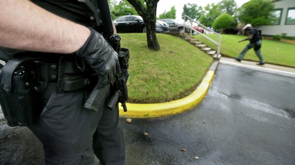 Em Little Rock, no Arkansas, EUA, um policial segura uma arma à esquerda enquanto outro agente de segurança patrulha a área ao fundo, em 20 de maio de 2015 - Sputnik Brasil