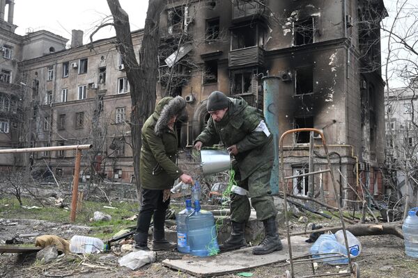 Combatente da Milícia Popular da República de Donetsk ajuda moradora de Mariupol a retirar água de poço na cidade - Sputnik Brasil