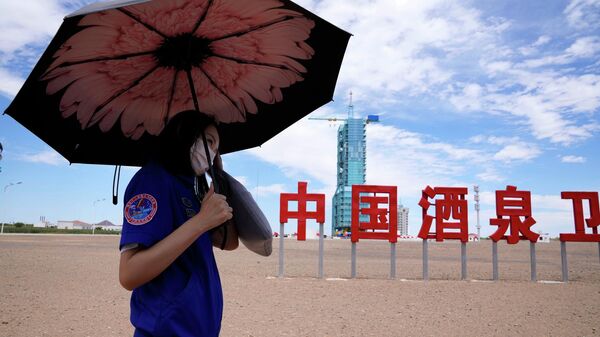 Um trabalhador segura um guarda-chuva perto da espaçonave Shenzhou-12 coberta na plataforma de lançamento perto de parte das palavras chinesas para Centro de Lançamento de Satélites China Jiuquan perto de Jiuquan, China, 16 de junho de 2021 - Sputnik Brasil