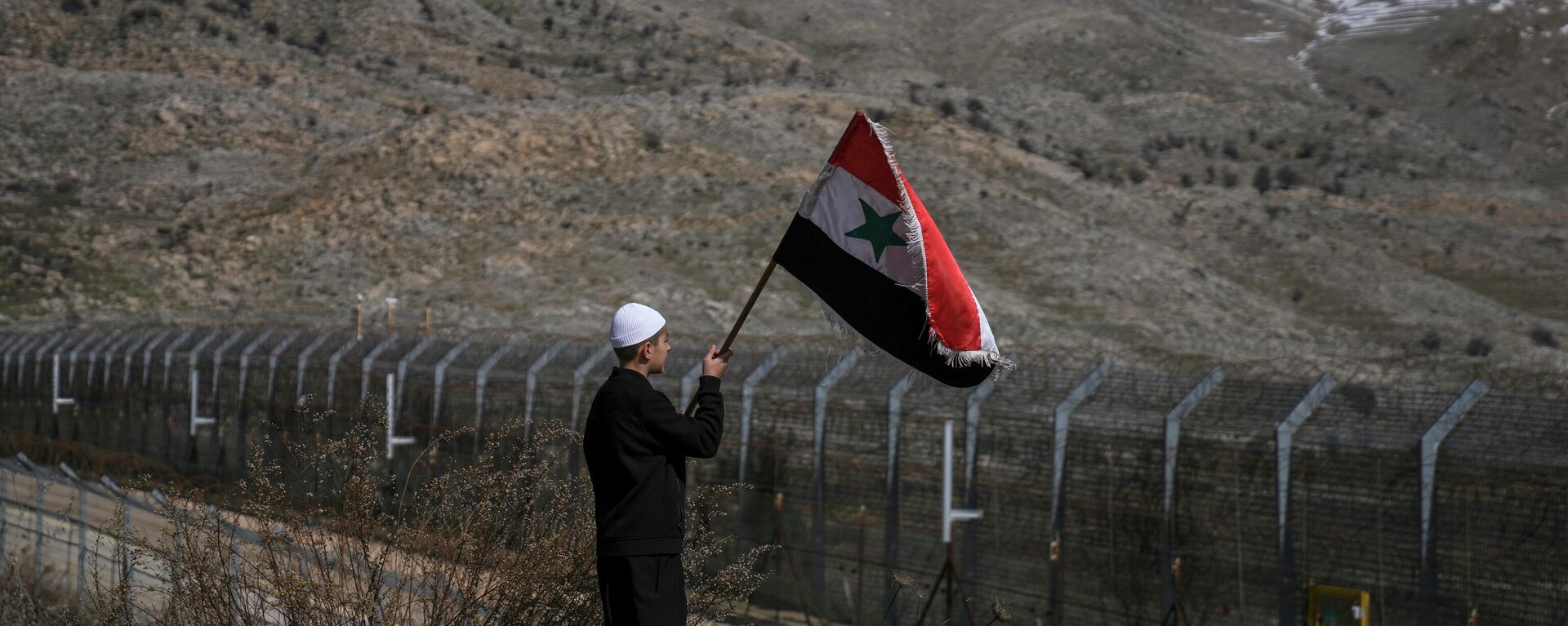 Um jovem agita uma bandeira da Síria durante uma manifestação pedindo o retorno à Síria das Colinas de Golã, 14 de fevereiro de 2022 - Sputnik Brasil, 1920, 11.04.2022