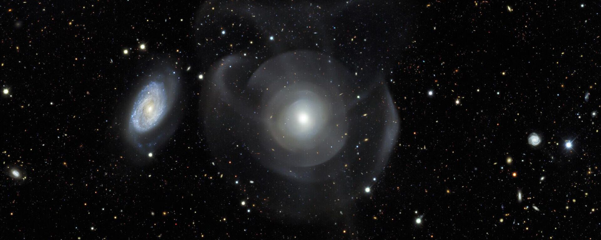 Galáxias elípticas como a NGC 474 são geralmente caracterizadas por sua aparência relativamente lisa quando comparadas com galáxias espirais (à esquerda), com estruturas floculentas entrelaçadas com faixas de poeira e braços espirais - Sputnik Brasil, 1920, 26.03.2023