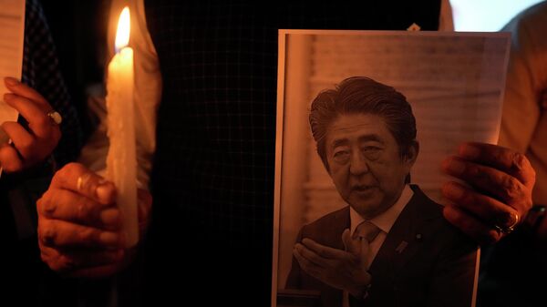 Homem segura uma vela e uma foto de Shinzo Abe durante uma reunião de oração - Sputnik Brasil