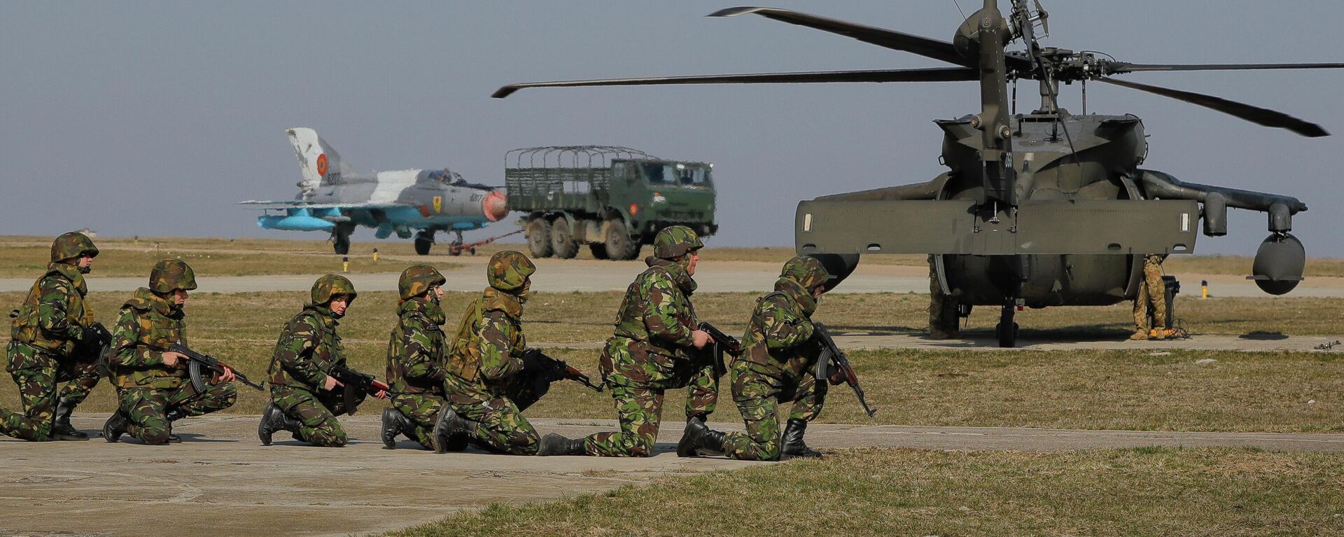 Com um jato de combate MIG 21 e um helicóptero Blackhawk ao fundo, soldados dos EUA participam de exercício militar conjunto com as Forças Armadas romenas na base aérea de Mihail Kogalniceanu, Romênia, 8 de março de 2017 - Sputnik Brasil, 1920, 14.07.2022