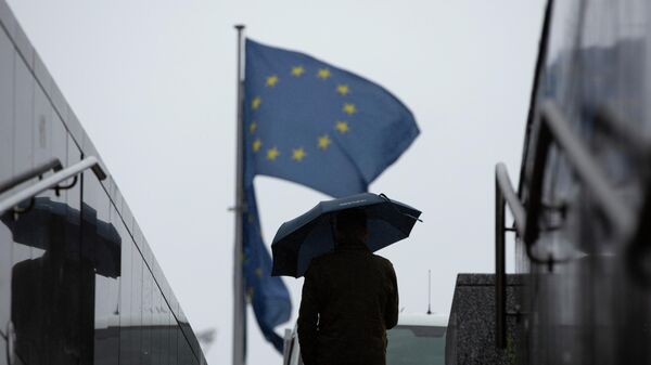 Homem caminha com guarda-chuva perto de bandeiras da União Europeia no exterior da sede do bloco, em Bruxelas, na Bélgica, em 16 de outubro de 2019 (foto de arquivo) - Sputnik Brasil