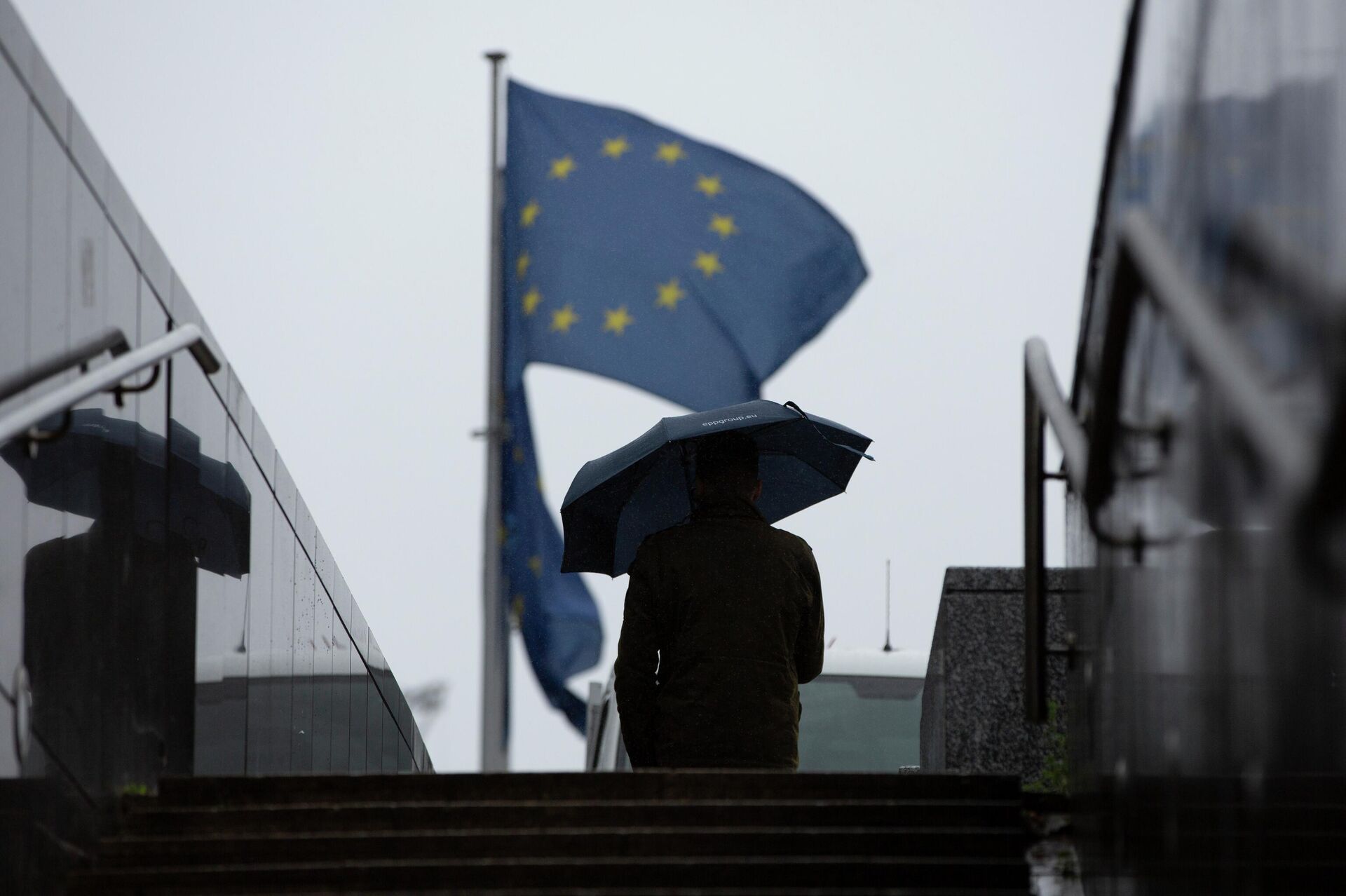 Homem caminha com guarda-chuva perto de bandeiras da União Europeia no exterior da sede do bloco, em Bruxelas, na Bélgica, em 16 de outubro de 2019 (foto de arquivo) - Sputnik Brasil, 1920, 29.07.2022