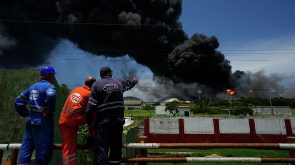 Trabalhadores do Sindicato Petrolífero de Cuba (CUPET, sigla em espanhol) observam uma enorme nuvem de fumaça que sai de uma instalação de petróleo, que pegou fogo após ser atingida por um raio, enquanto bombeiros trabalham para conter o incêndio, em Matanzas, em Cuba, em 6 de agosto de 2022 - Sputnik Brasil