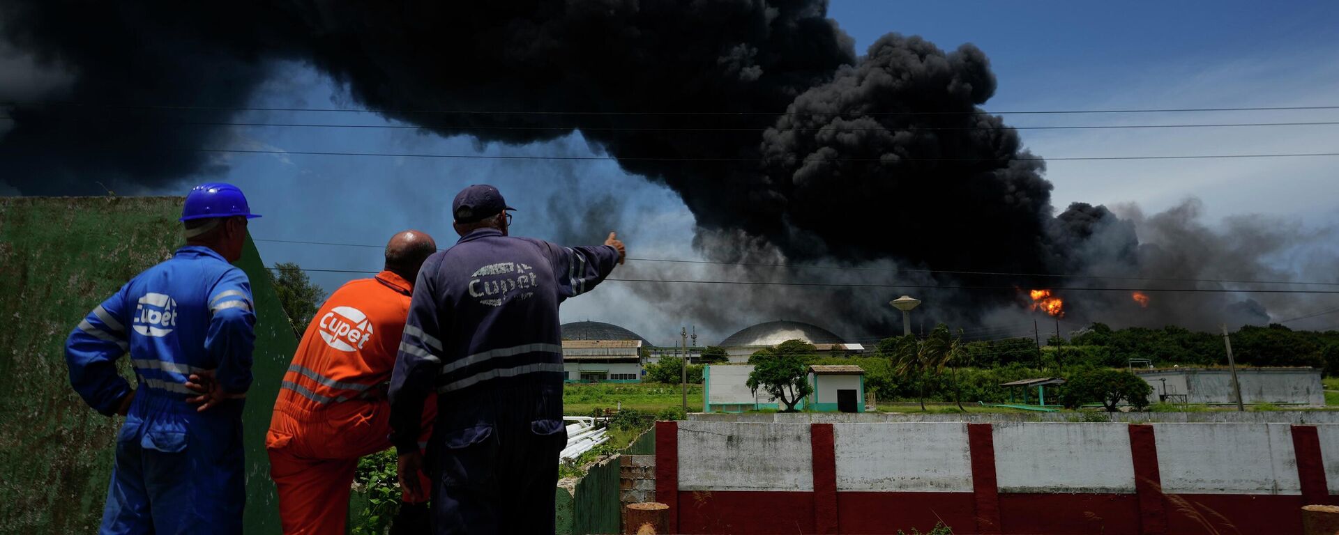 Trabalhadores do Sindicato Petrolífero de Cuba (CUPET, sigla em espanhol) observam uma enorme nuvem de fumaça que sai de uma instalação de petróleo, que pegou fogo após ser atingida por um raio, enquanto bombeiros trabalham para conter o incêndio, em Matanzas, em Cuba, em 6 de agosto de 2022 - Sputnik Brasil, 1920, 07.08.2022