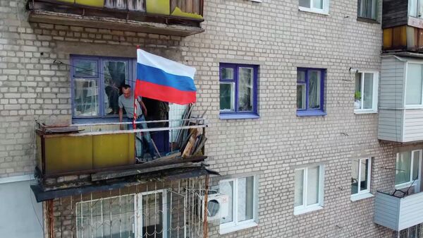 Homem coloca bandeira russa na varanda de edifício residencial em Lisichansk, na República Popular de Lugansk (RPL), em 4 de julho de 2022 - Sputnik Brasil