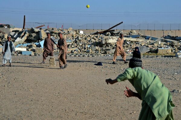 Meninos jogam críquete na frente de uma escola que foi danificada durante o conflito entre o Talibã e o antigo governo do Afeganistão, em Kandahar, 12 de maio de 2022. - Sputnik Brasil
