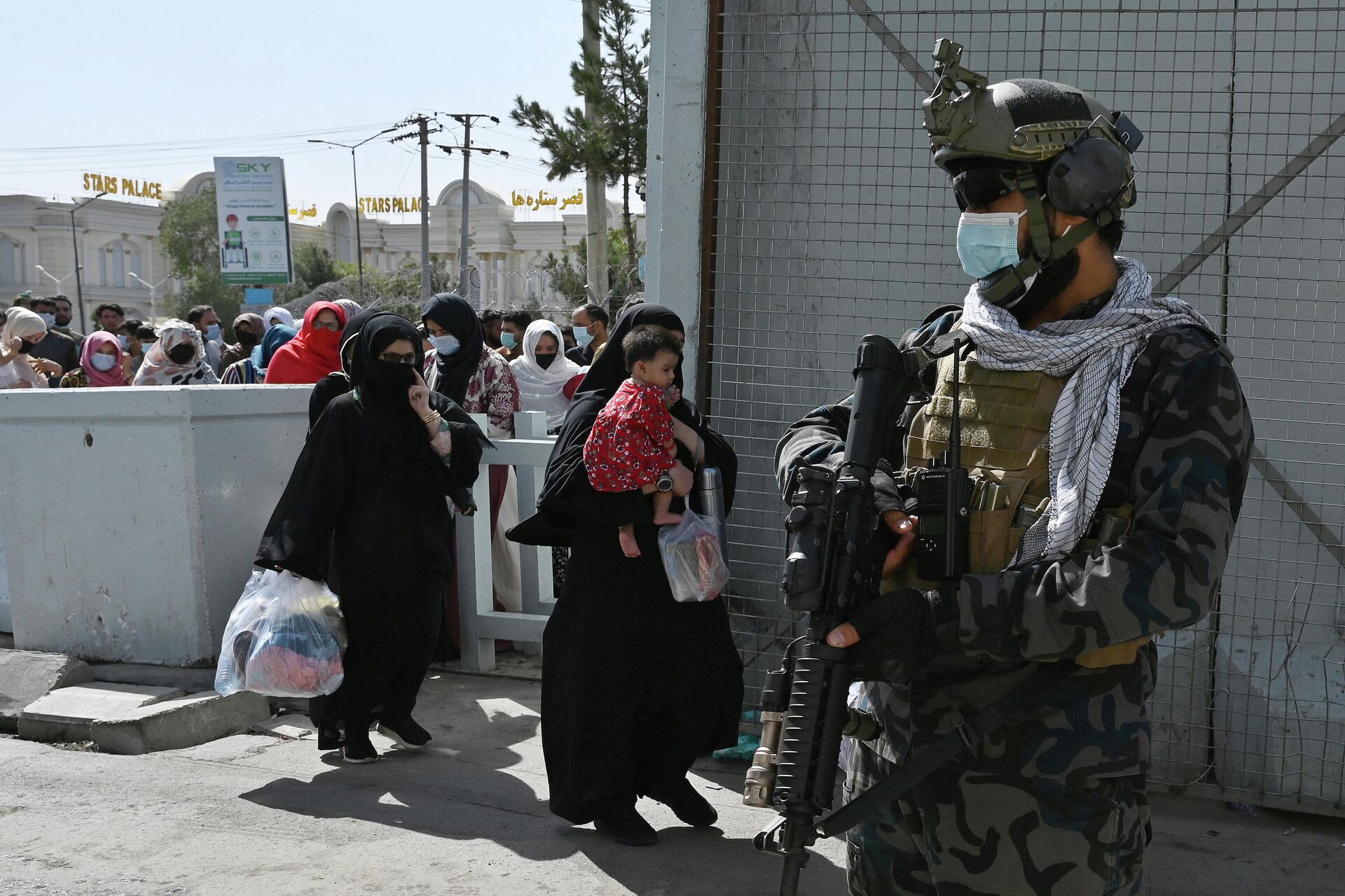 Combatentes de uma unidade de forças especiais do Talibã (grupo sob sanções da ONU por atividades terroristas), montam guarda enquanto afegãos, que aguardam para deixar o Afeganistão, atravessam o portão de entrada principal do aeroporto de Cabul, em 28 de agosto de 2021 - Sputnik Brasil, 1920, 01.09.2022