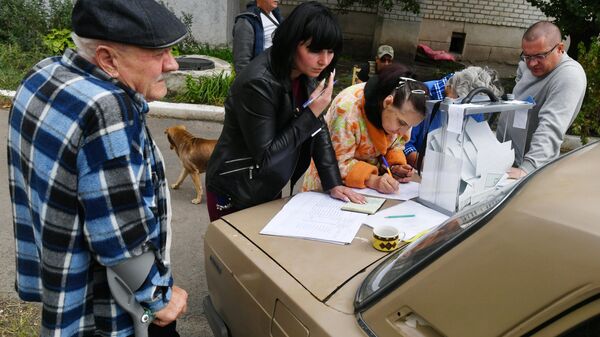 Moradores de Volnovakha, na República Popular de Donetsk, votam no referendo em urna portátil conduzida por funcionários da comissão eleitoral a fim de evitar aglomerações nos locais de votação, em 24 de setembro de 2022 - Sputnik Brasil