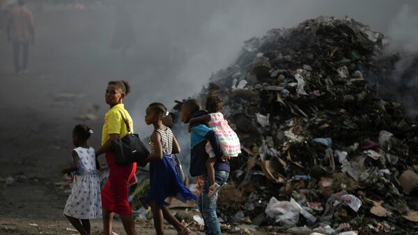 Mulher acompanhada dos filhos caminha perto de pilha de lixo fumegante em Porto Príncipe, capital do Haiti, em 28 de setembro de 2002 - Sputnik Brasil
