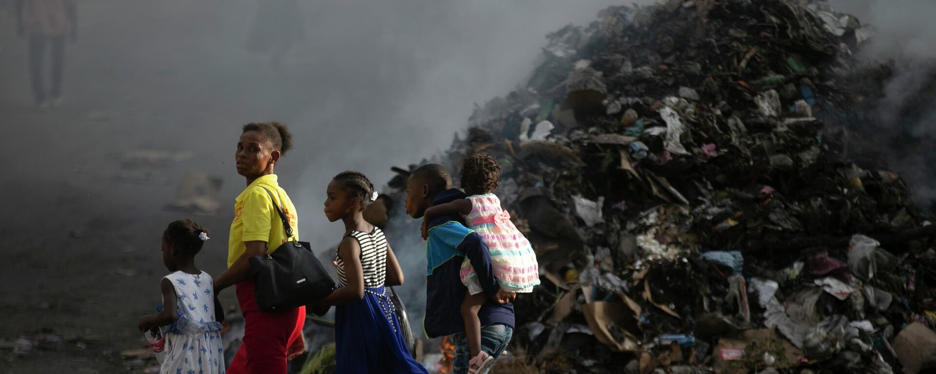 Mulher acompanhada dos filhos caminha perto de pilha de lixo fumegante em Porto Príncipe, capital do Haiti, em 28 de setembro de 2002 - Sputnik Brasil, 1920, 08.03.2024