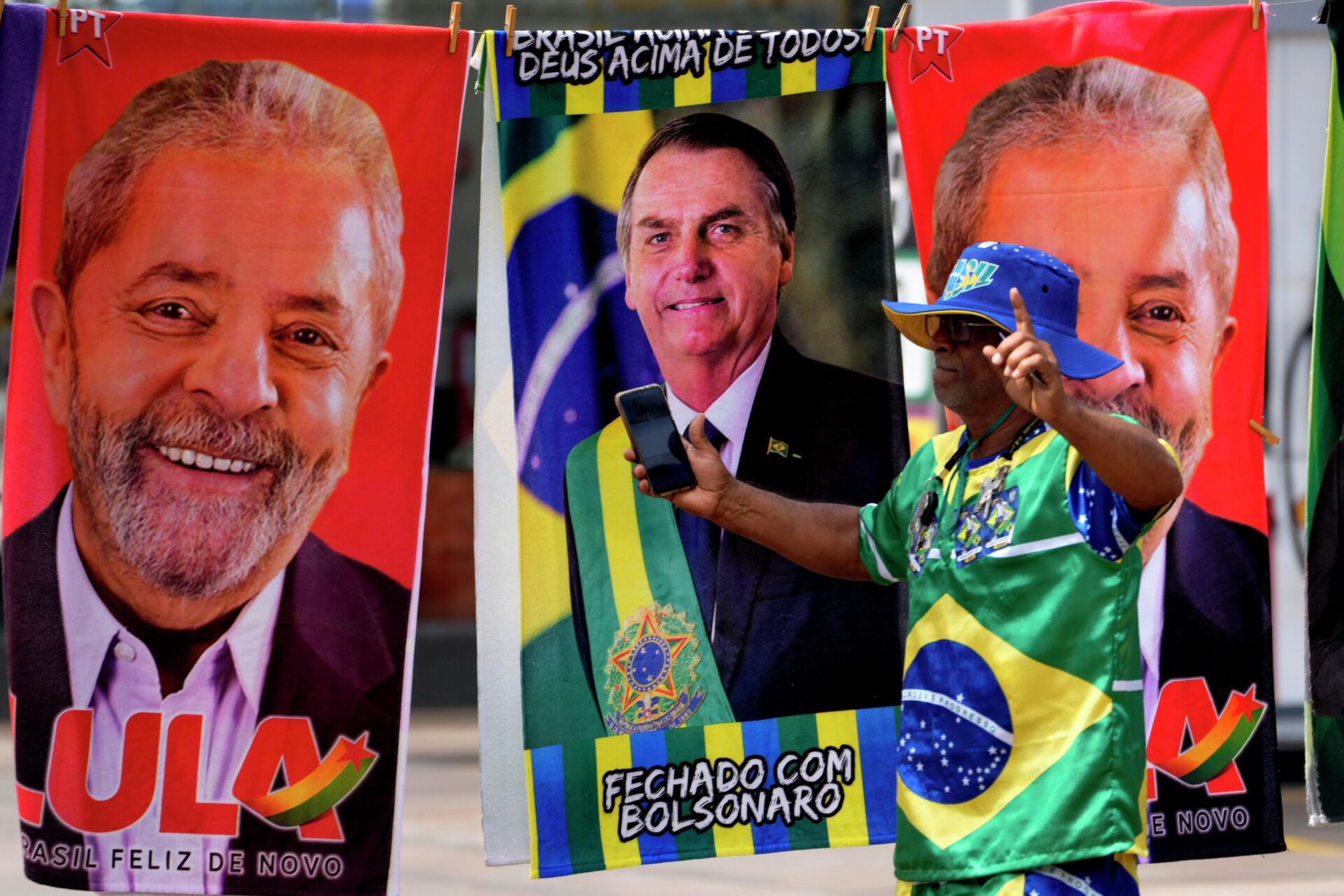 Apoiador vestido com as cores da bandeira do Brasil passa em frente a toalhas à venda com os rostos dos candidatos à Presidência Jair Bolsonaro (PL) e Luiz Inácio Lula da Silva (PT). Brasília, 23 de setembro de 2022 - Sputnik Brasil, 1920, 14.10.2022