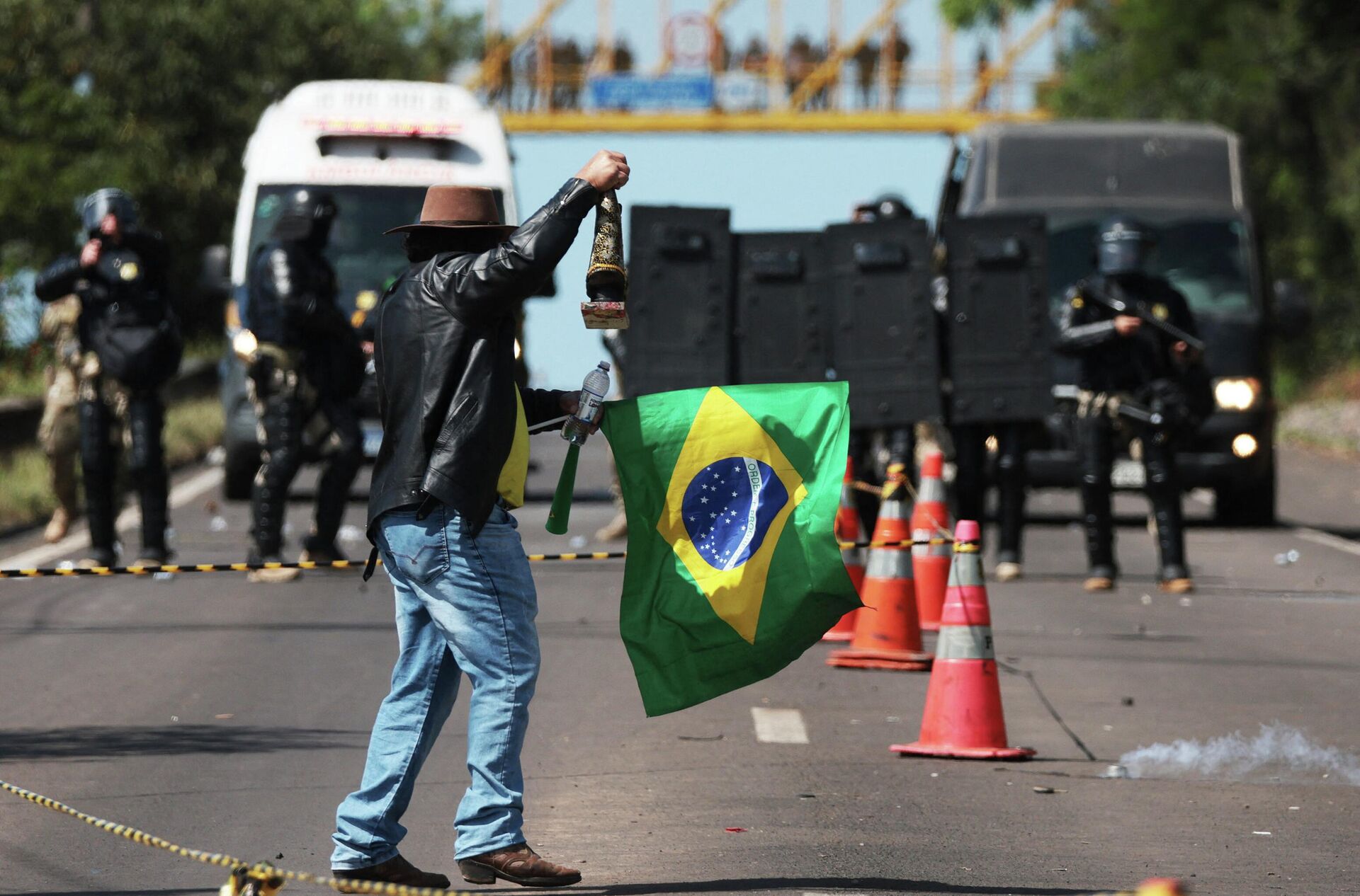 Apoiador do presidente Jair Bolsonaro (PL) segura bandeira brasileira e imagem religiosa enquanto enfrenta a tropa de choque da Polícia Militar, que tenta dispersar manifestantes, durante bloqueio na rodovia BR-116 em Novo Hamburgo (RS), em 1º de novembro de 2022 - Sputnik Brasil, 1920, 01.11.2022