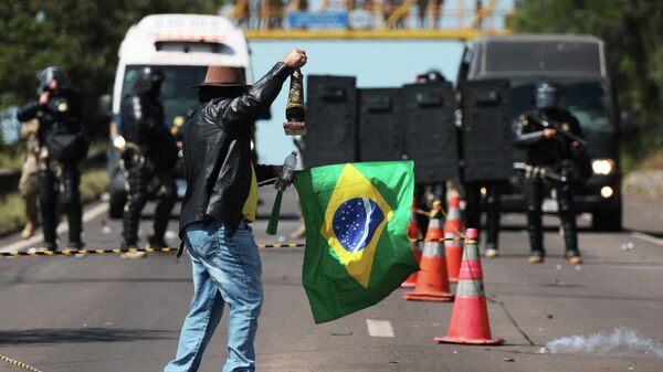 Apoiador do presidente Jair Bolsonaro (PL) segura bandeira brasileira e imagem religiosa enquanto enfrenta a tropa de choque da Polícia Militar, que tenta dispersar manifestantes, durante bloqueio na rodovia BR-116 em Novo Hamburgo (RS), em 1º de novembro de 2022 - Sputnik Brasil