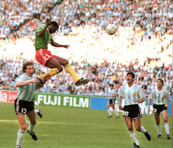 O atacante camaronês François Omam-Biyick marca gol de cabeça enquanto os zagueiros argentinos Nestor Lorenzo (à esquerda) e Juan Simon ficam observando, em 8 de junho de 1990 em Milão, durante partida de abertura da Copa do Mundo entre Camarões e Argentina. - Sputnik Brasil