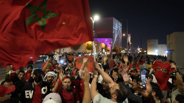 Um homem agita uma bandeira marroquina, enquanto as pessoas comemoram em Doha, Catar, depois que o Marrocos venceu Portugal nas quartas de final da Copa do Mundo, no sábado, 10 de dezembro de 2022 - Sputnik Brasil