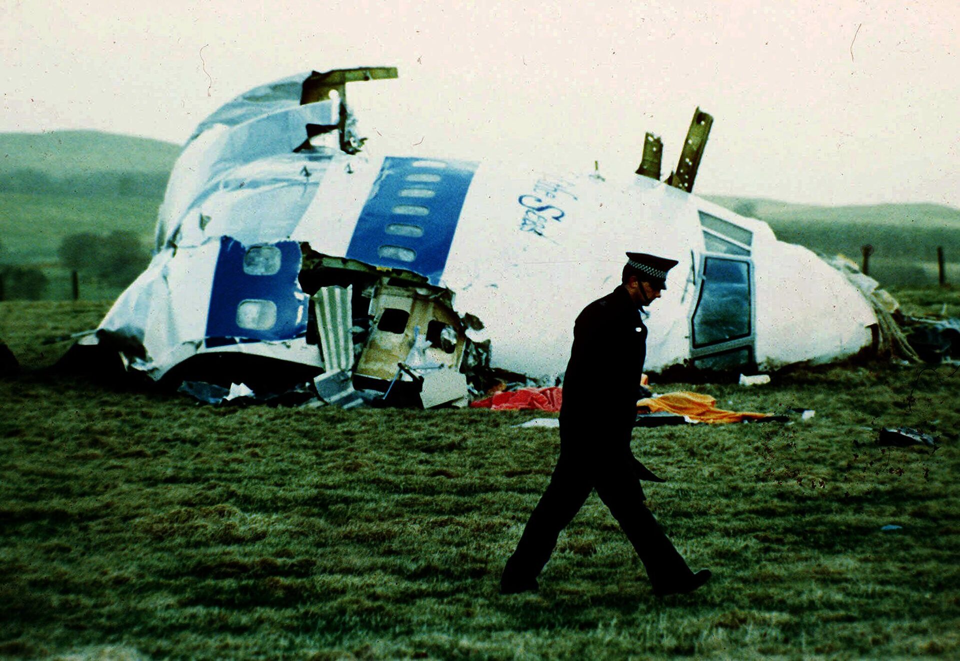Policial caminha perto do avião 103 da Pan Am, em um campo perto da cidade de Lockerbie, na Escócia, onde estava depois que uma bomba a bordo explodiu, matando um total de 270 pessoas, na quarta-feira, 21 de dezembro de 1988 - Sputnik Brasil, 1920, 11.12.2022