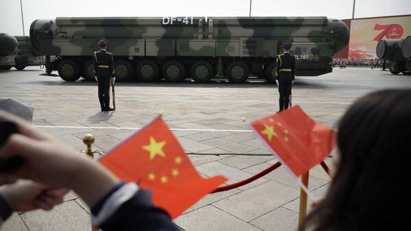 Espectadores agitam bandeiras chinesas enquanto observam passagem de veículos militares carregando mísseis balísticos DF-41 capazes de usar ogivas nucleares em parada comemorativa do 70º aniversário da República Popular da China em Pequim, China, 1º de outubro de 2019 - Sputnik Brasil