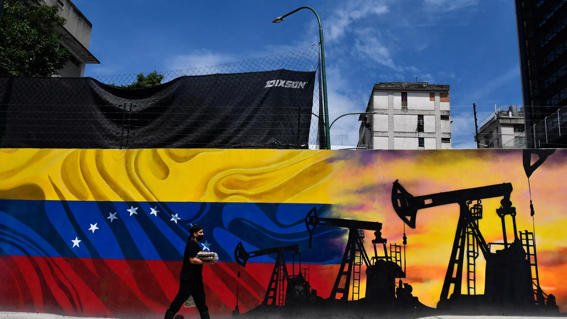 Um homem usando uma máscara facial passa por um mural representando uma bomba de petróleo e a bandeira venezuelana em uma rua de Caracas, em 26 de maio de 2022 - Sputnik Brasil, 1920, 07.07.2023