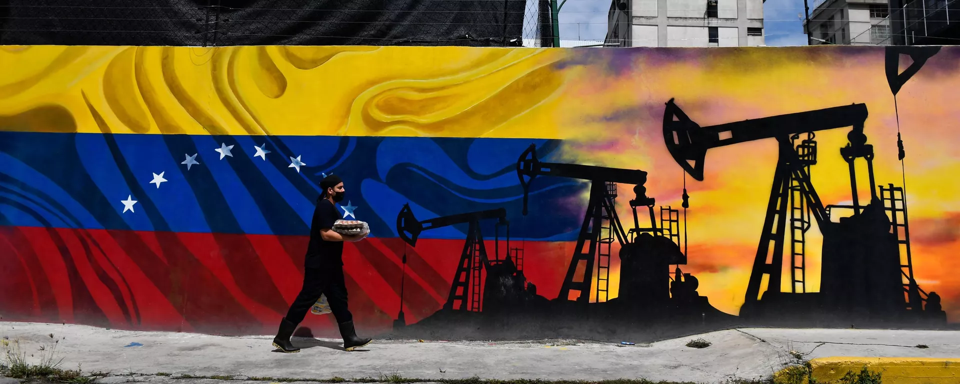 Um homem usando uma máscara facial passa por um mural representando uma bomba de petróleo e a bandeira venezuelana em uma rua de Caracas, em 26 de maio de 2022 - Sputnik Brasil, 1920, 07.07.2023