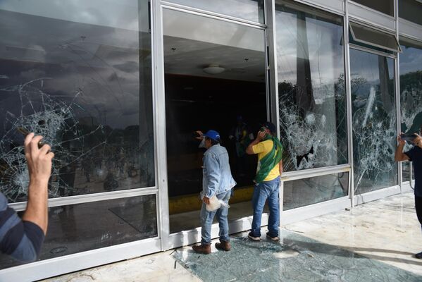 Manifestantes bolsonaristas diante de vidraças destruídas no Supremo Tribunal Federal, em meio à invasão da praça dos Três Poderes e de prédios públicos na capital brasileira. Brasília, Distrito Federal, 8 de janeiro de 2023 - Sputnik Brasil