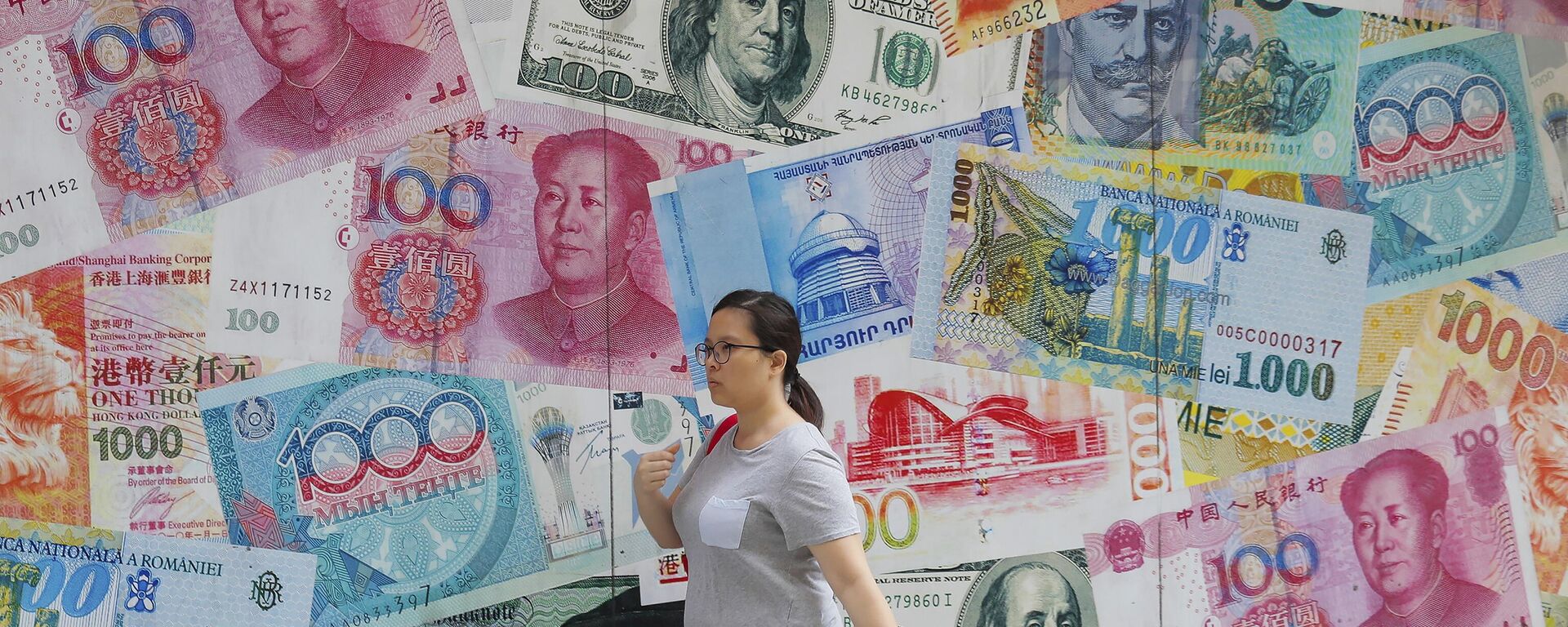 Uma mulher passa por uma casa de câmbio decorada com notas de moedas de diferentes países no Central, um distrito comercial de Hong Kong, 6 de agosto de 2019 - Sputnik Brasil, 1920, 09.01.2023