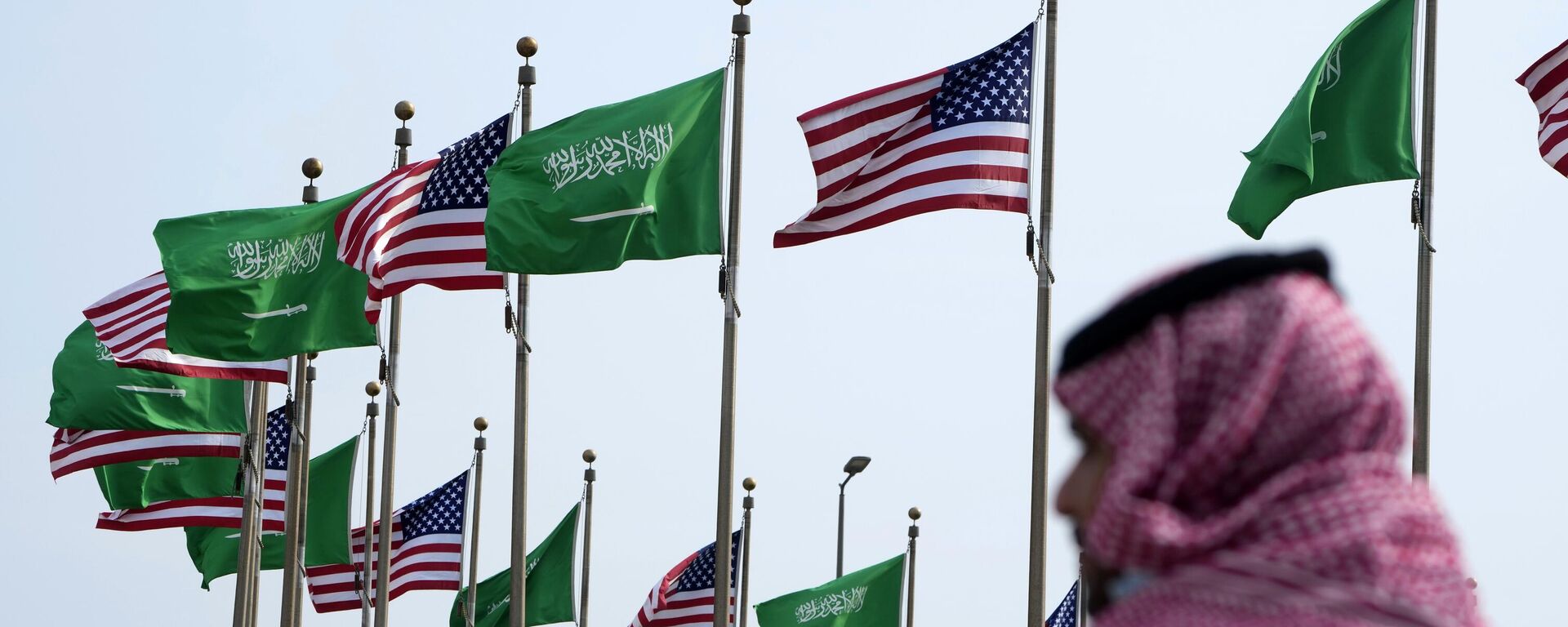 Homem caminha próximo das bandeiras da Arábia Saudita e dos EUA - Sputnik Brasil, 1920, 04.04.2023