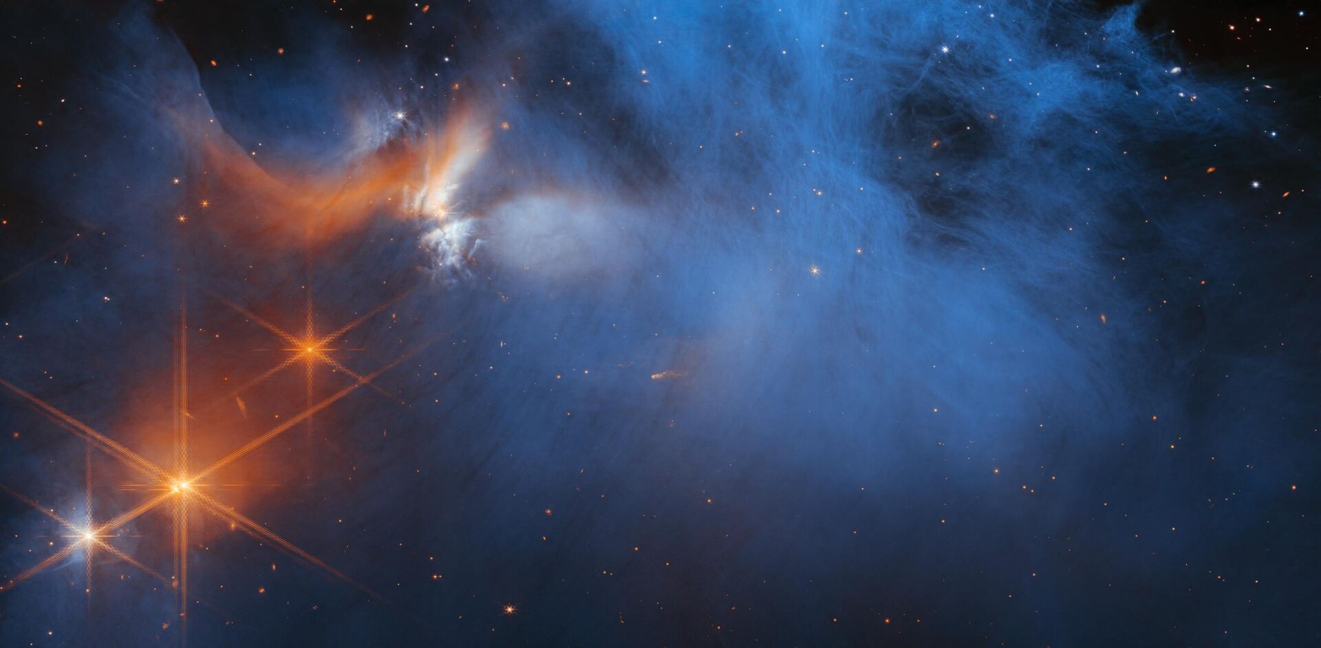 Esta imagem representa a região central da nuvem molecular escura de Camaleão I, que se encontra a 630 anos-luz de distância. O material frio e suave das nuvens (em azul, ao centro) está iluminado no infravermelho pelo brilho da jovem protoestrela Ced 110 IRS 4 (em laranja, à esquerda). A luz de inúmeras estrelas no fundo é vista na cor alaranjada atrás da nuvem - Sputnik Brasil, 1920, 24.01.2023