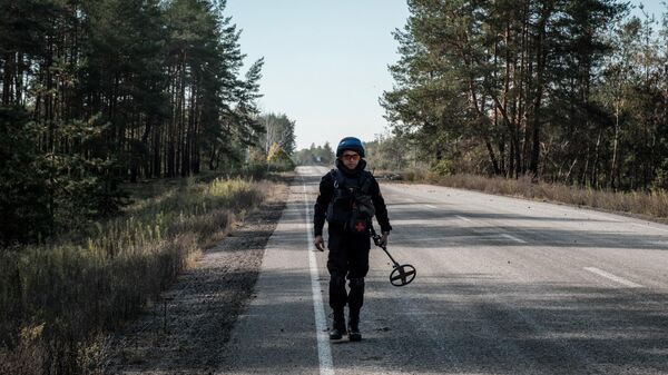 Um oficial da equipe de desminagem de emergência da polícia nacional ucraniana usa um detector de metais para procurar minas ao longo da estrada perto da cidade recentemente retomada de Lyman, na região de Donetsk, em 6 de outubro de 2022, em meio à invasão russa da Ucrânia - Sputnik Brasil
