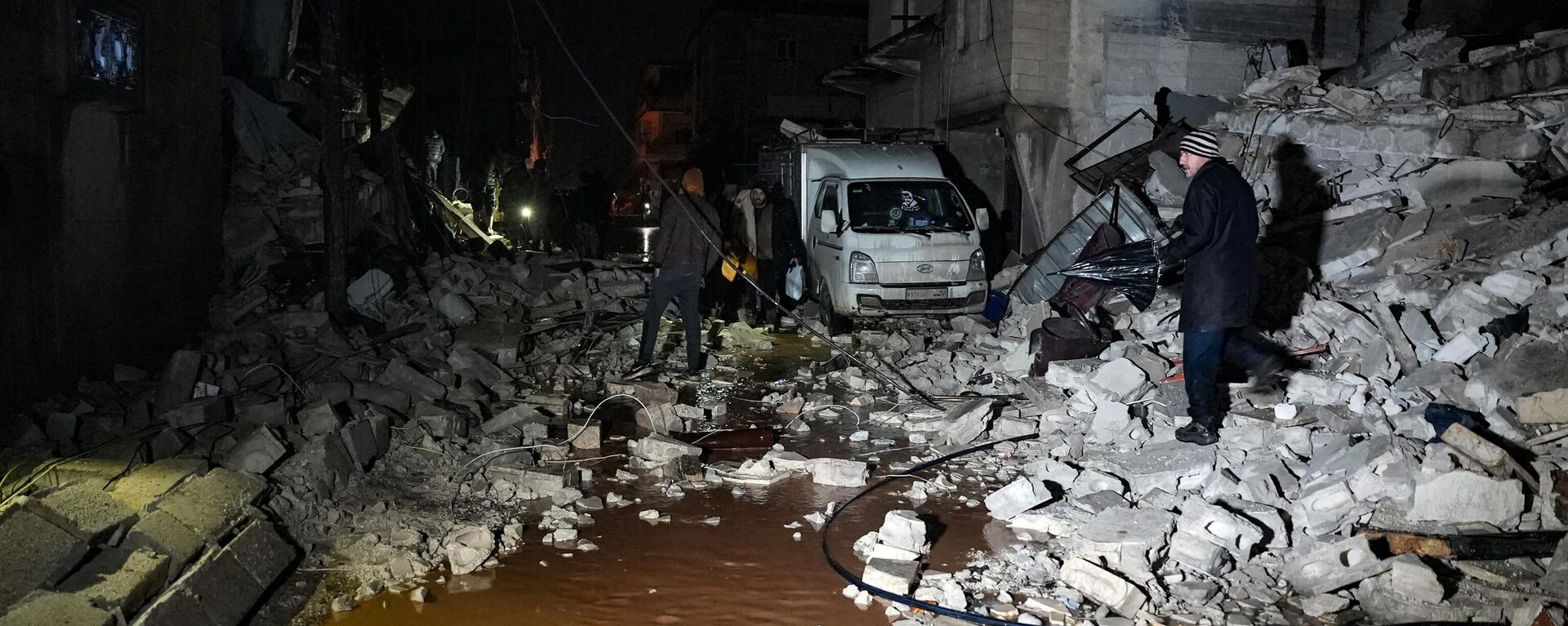 Moradores caminham entre escombros de edifícios desmoronados após um terremoto ter provocado destruição na cidade de Jandaris, distrito de Afrin, no noroeste da Síria - Sputnik Brasil, 1920, 06.02.2023
