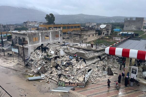 Pessoas vasculham os destroços de um prédio que desmoronou na cidade de Azmarin, na província síria de Idlib, no norte do país. - Sputnik Brasil
