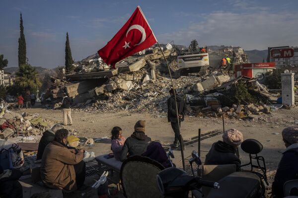 Família sentada junto de prédio colapsado após terremoto, Antália, Turquia, 11 de fevereiro de 2023. - Sputnik Brasil